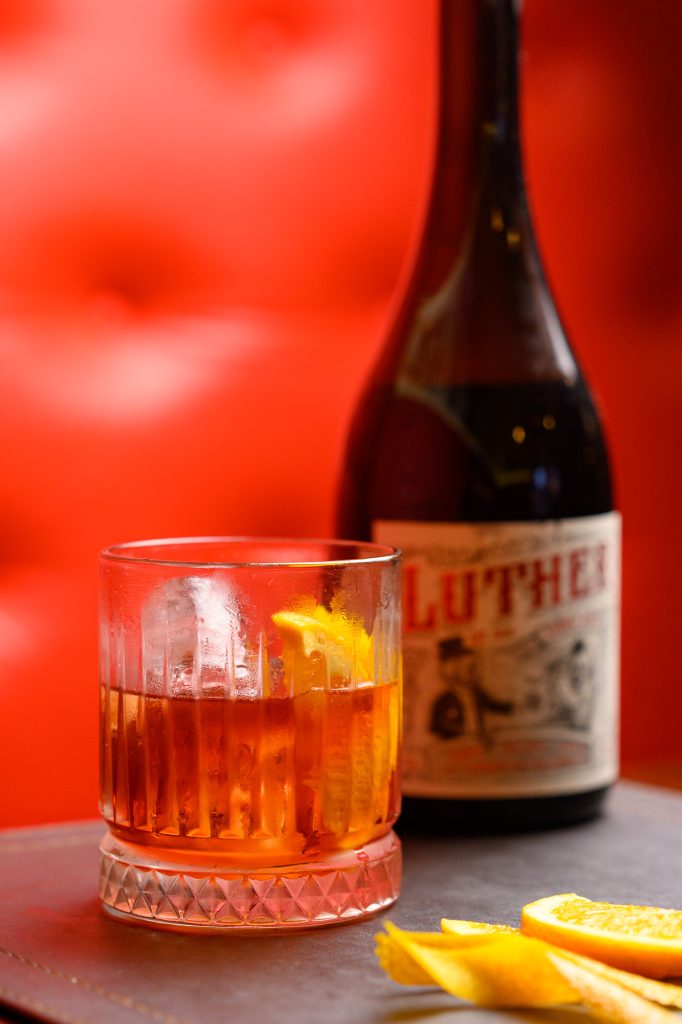 Negroni de la Casa sobre hielo con twist de naranja, junto a una botella de vermut Luther